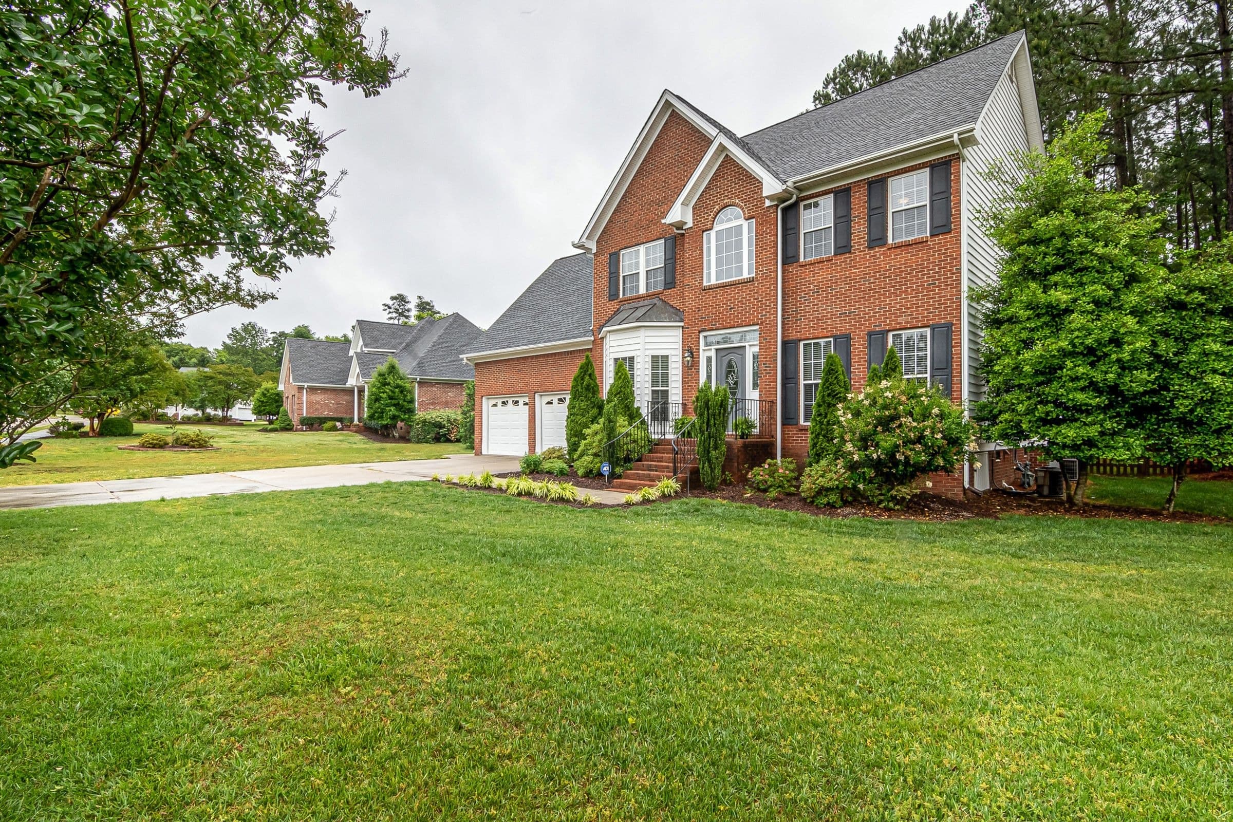 Two-story red brick house with a green lawn and tall pines