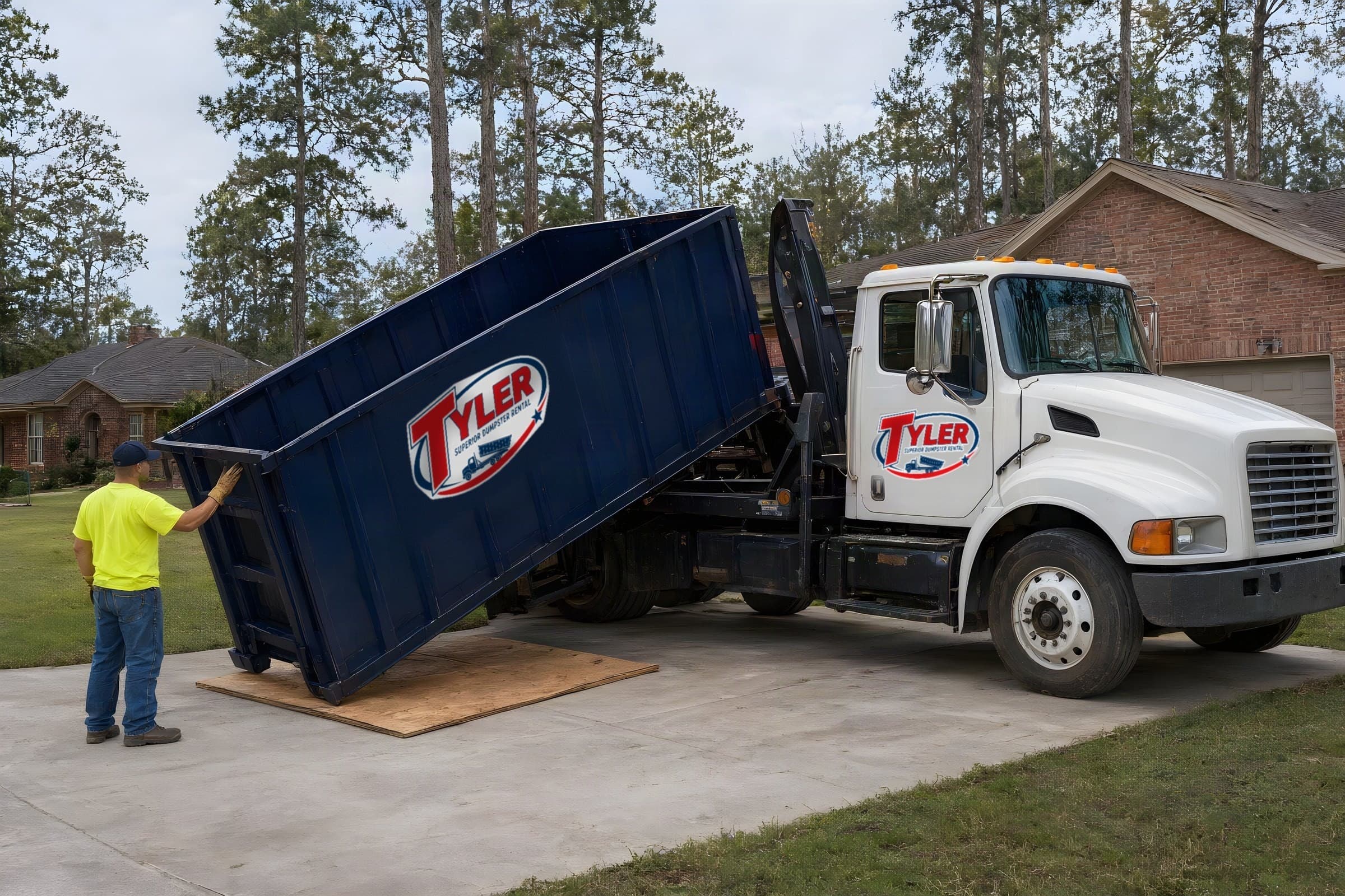 Roll-off truck sliding a navy 20 yard dumpster onto plywood boards in a Tyler driveway